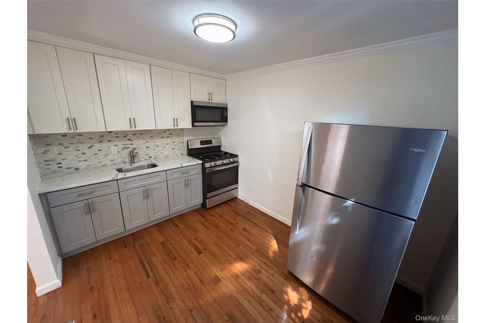 Kitchen with appliances with stainless steel finishes, gray cabinets, ornamental molding, decorative backsplash, and dark wood finished floors