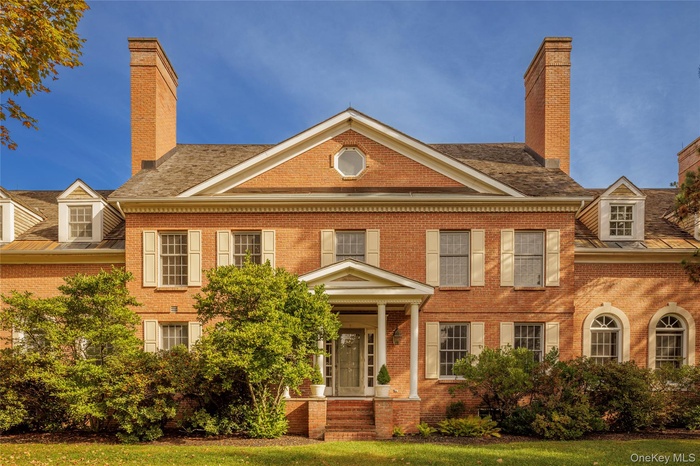 Colonial house with brick siding, a chimney, and a front lawn