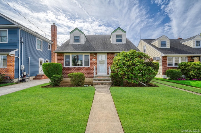 Cape cod home with a front lawn, roof with shingles, and brick siding