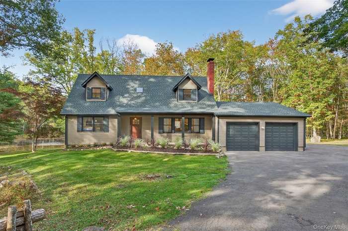 Cape cod-style house featuring a front lawn, covered porch, asphalt driveway, and an attached garage