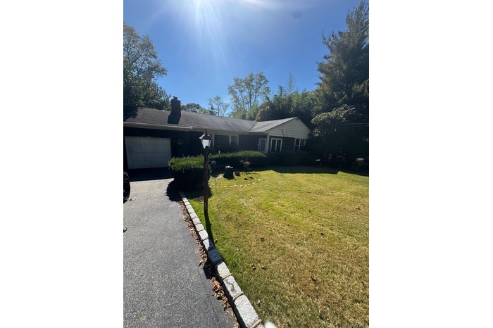 Ranch-style home featuring a front lawn, a chimney, an attached garage, and asphalt driveway