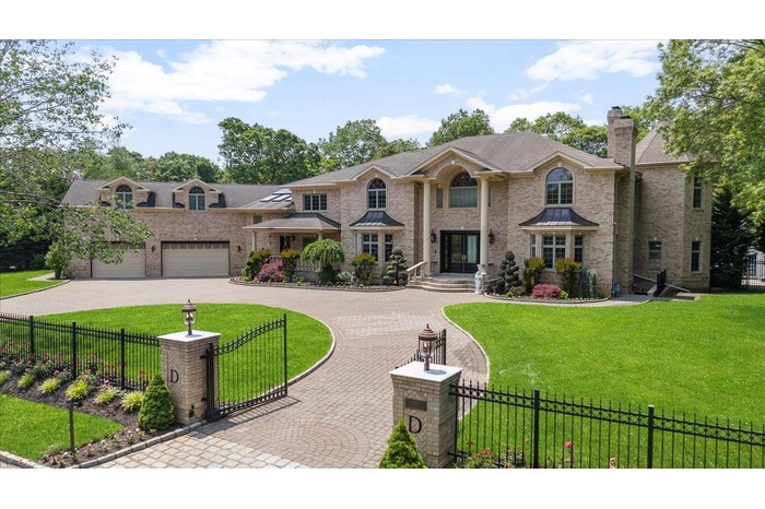 View of front of house featuring curved driveway, a chimney, brick siding, and a gate
