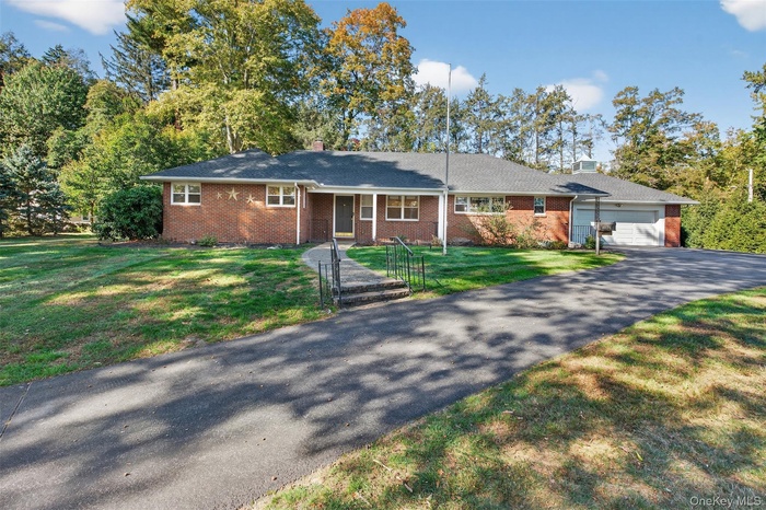 Single story home featuring brick siding, driveway, a front yard, an attached garage, and a chimney
