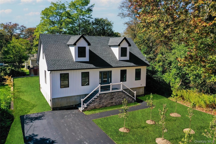 View of front facade featuring a front yard, a shingled roof, and stairs