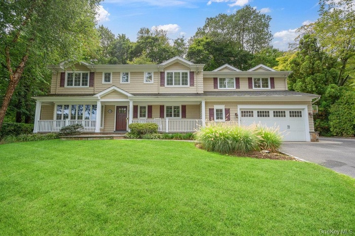 View of front of home with covered porch, asphalt driveway, a front yard, and a garage