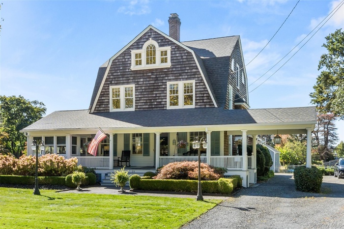 View of front of house featuring a porch, a gambrel roof, roof with shingles, and a front yard