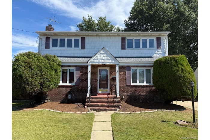 View of front of home featuring a front lawn, roof with shingles, and brick siding