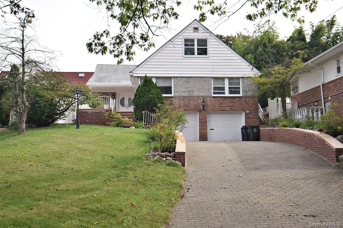 View of front of property with decorative driveway, brick siding, a front yard, and an attached garage