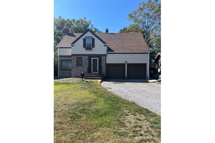 View of front of house with a front lawn, a chimney, gravel driveway, and an attached garage