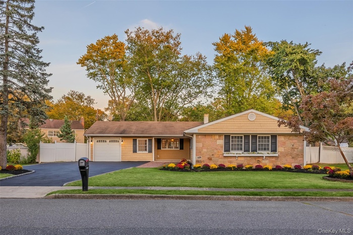 Single story home featuring asphalt driveway, a garage, a chimney, and stone siding