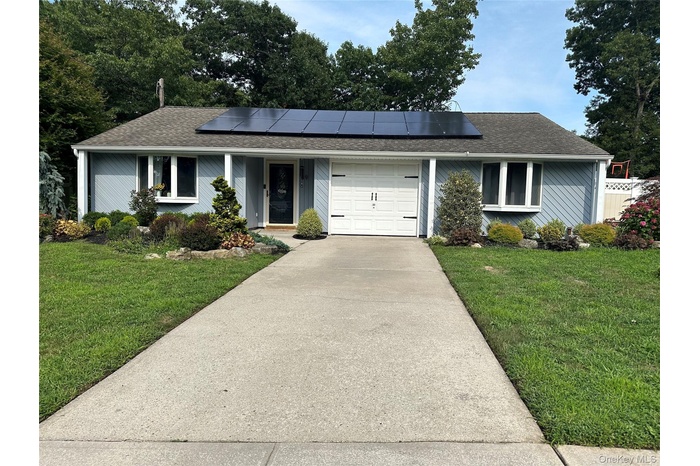 Single story home with a shingled roof, a front yard, driveway, and roof mounted solar panels