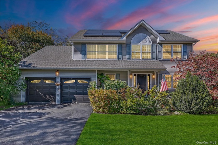 Traditional-style house with driveway, roof with shingles, and roof mounted solar panels