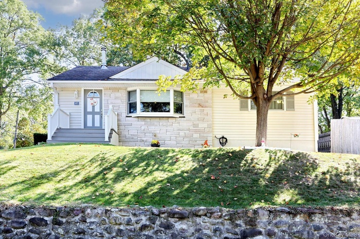 Single story home with stone siding, a front lawn, and roof with shingles