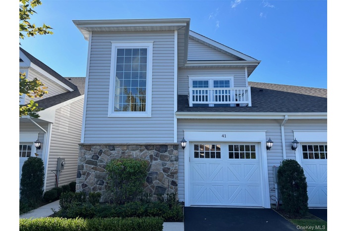 View of front of property with a garage, a balcony, a shingled roof, driveway, and stone siding