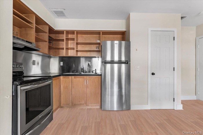 Kitchen featuring appliances with stainless steel finishes, dark countertops, open shelves, light wood-style flooring, and under cabinet range hood