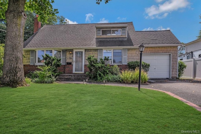View of front facade featuring a garage, a front lawn, a chimney, roof with shingles, and asphalt driveway