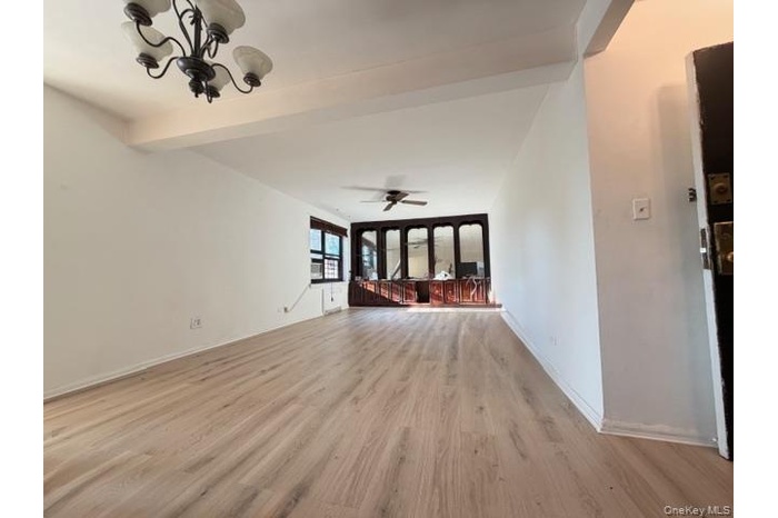 Unfurnished living room featuring beam ceiling, light wood finished floors, a chandelier, and a ceiling fan