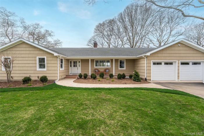Single story home featuring driveway, a chimney, a shingled roof, a front yard, and an attached garage
