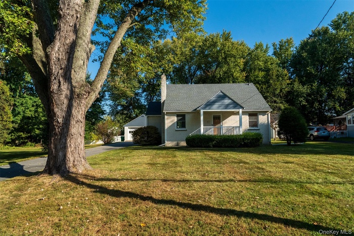 View of front facade featuring a porch, a front lawn, a chimney, brick siding, and driveway