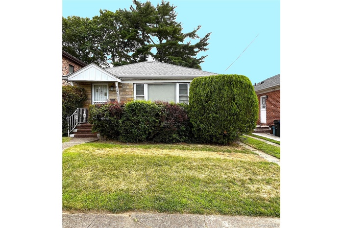 View of front of property with a front yard, stone siding, and a shingled roof