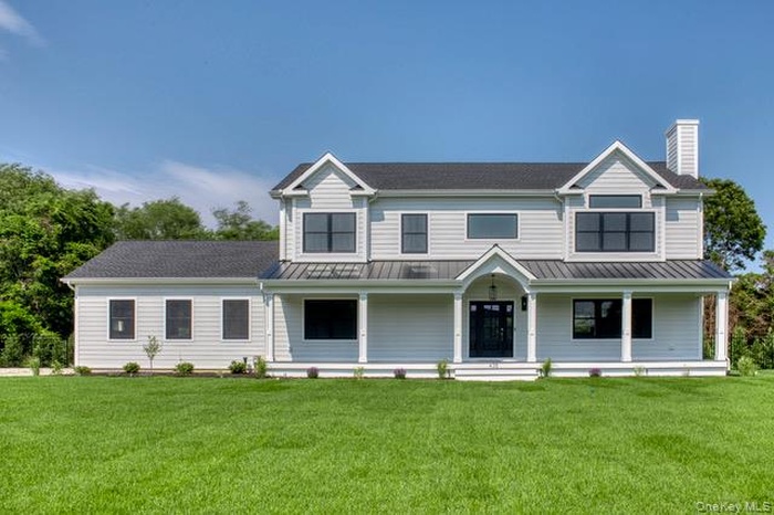 View of front of house with covered porch, a front yard, a chimney, a standing seam roof, and a metal roof