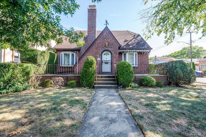 Charming Cape with brick siding, a chimney, a front yard, and roof with shingles