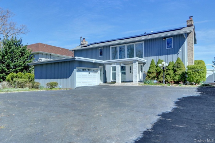 View of front of home with a chimney, solar panels, asphalt driveway, and an attached garage