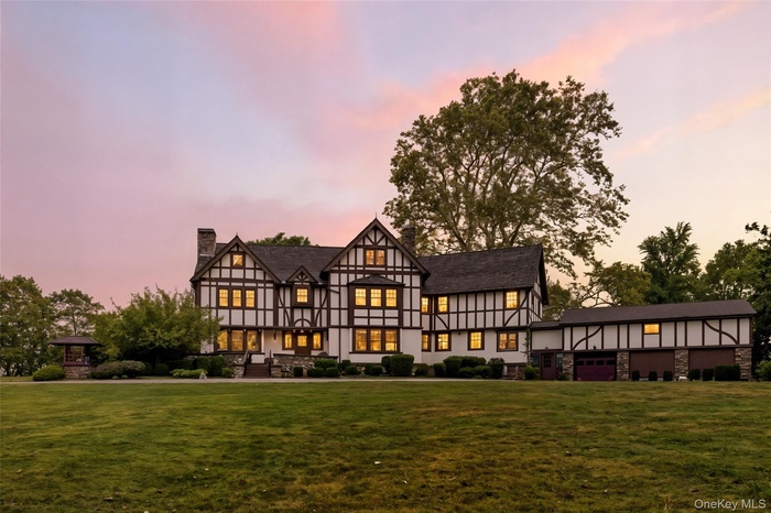 Back of property at dusk with a chimney, a lawn, and stone siding