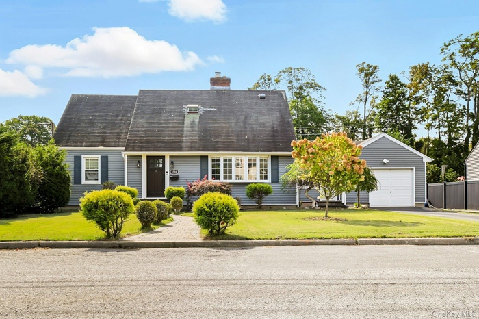 Cape cod-style house featuring a front lawn, a garage, a chimney, and driveway