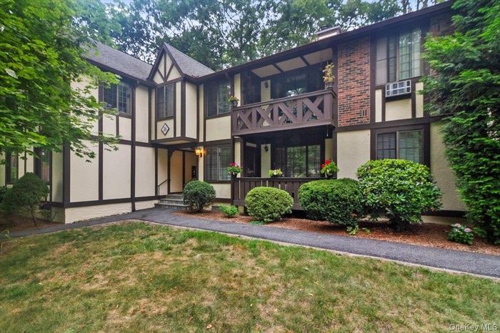 Tudor-style house with stucco siding, a balcony, a front yard, and a chimney