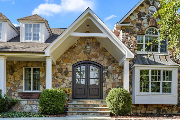 Entrance to property featuring stone siding, covered porch, and a shingled roof