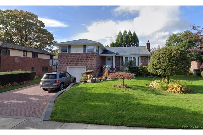 Split level home with decorative driveway, brick siding, a chimney, a front lawn, and a garage