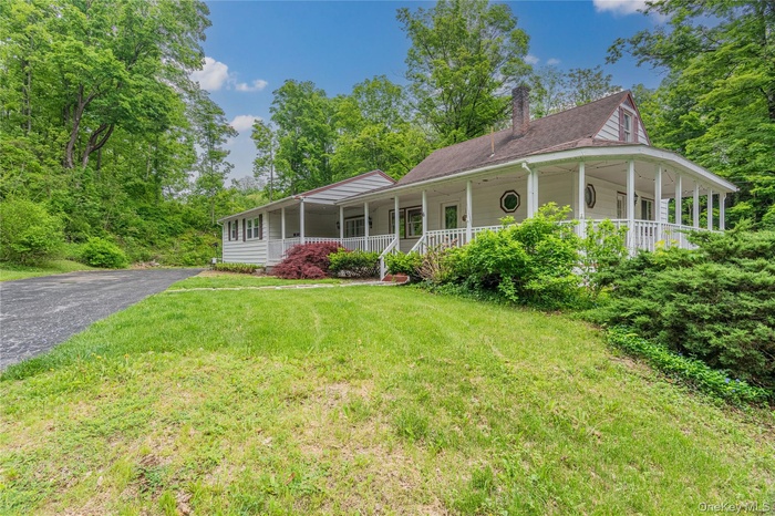Farmhouse-style home featuring a porch, a front lawn, a chimney, and driveway