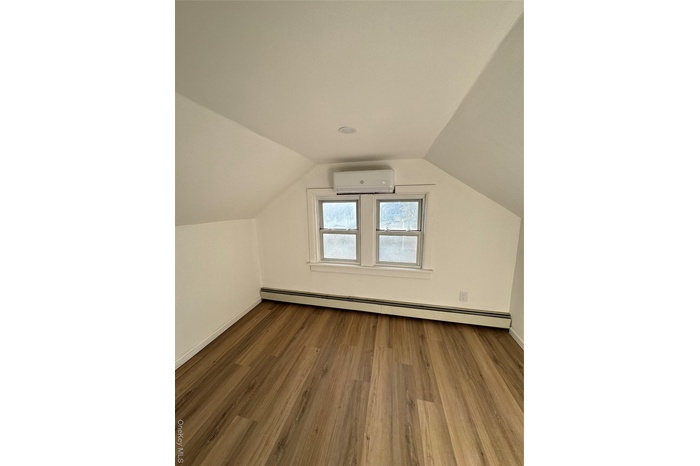 Bonus room featuring wood finished floors, a baseboard heating unit, vaulted ceiling, and a wall unit AC