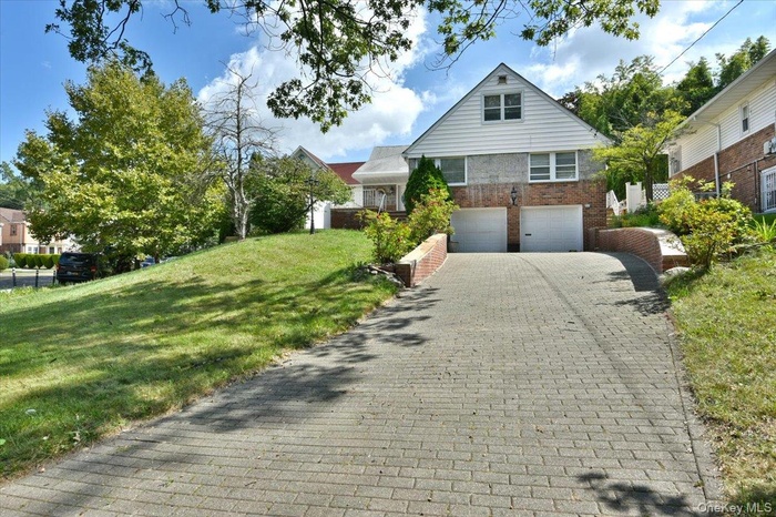 View of front of property with decorative driveway, brick siding, a garage, and a front lawn