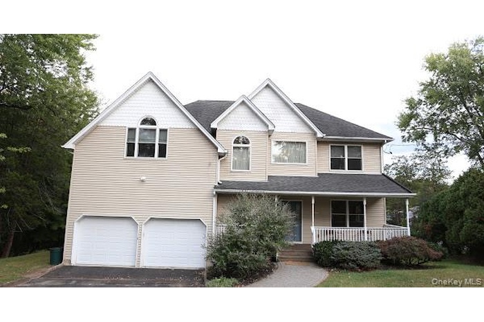 View of front of property featuring a porch, asphalt driveway, an attached garage, and a shingled roof