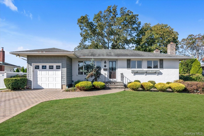 Ranch-style house with a front lawn, an attached garage, a chimney, decorative driveway, and brick siding