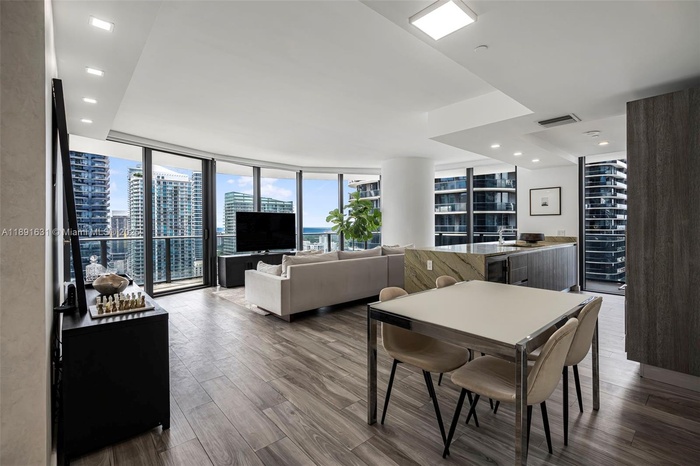 Bright open-concept dining and living space with floor-to-ceiling windows, upgraded marble kitchen island, and panoramic Brickell skyline and bay view
