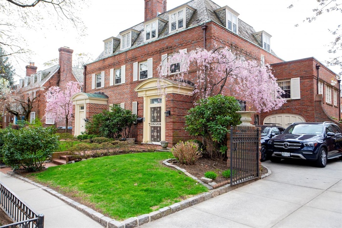 View of front of house featuring a front lawn, mansard roof, concrete driveway, brick siding, and a high end roof