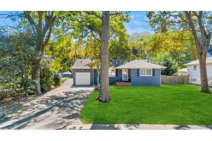 View of front of property with driveway, a shingled roof, a garage, and view of scattered trees