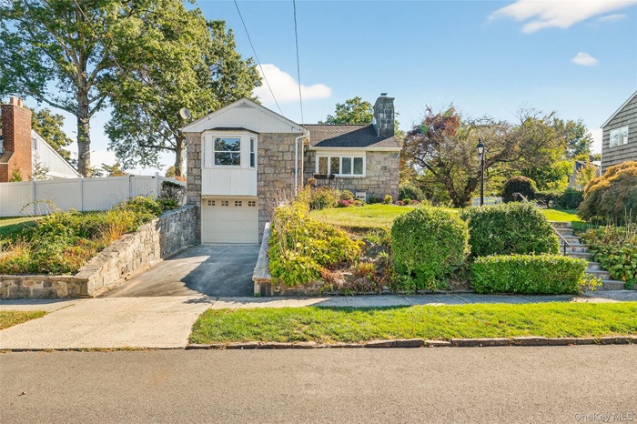 View of front of home featuring stone siding, driveway, an attached garage, and a chimney