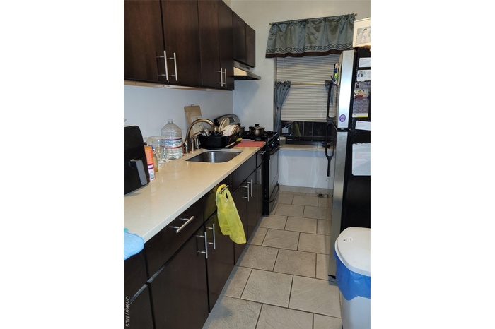Kitchen with refrigerator, light tile patterned floors, black range with gas stovetop, extractor fan, and light stone countertops
