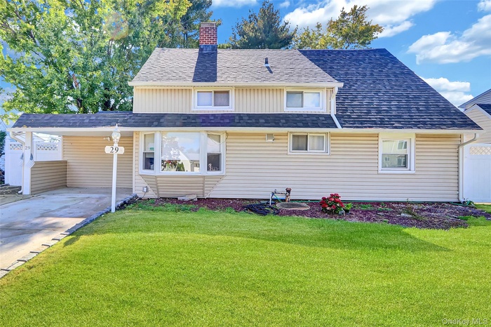 View of front of home with a front lawn, roof with shingles, a chimney, an attached carport, and driveway