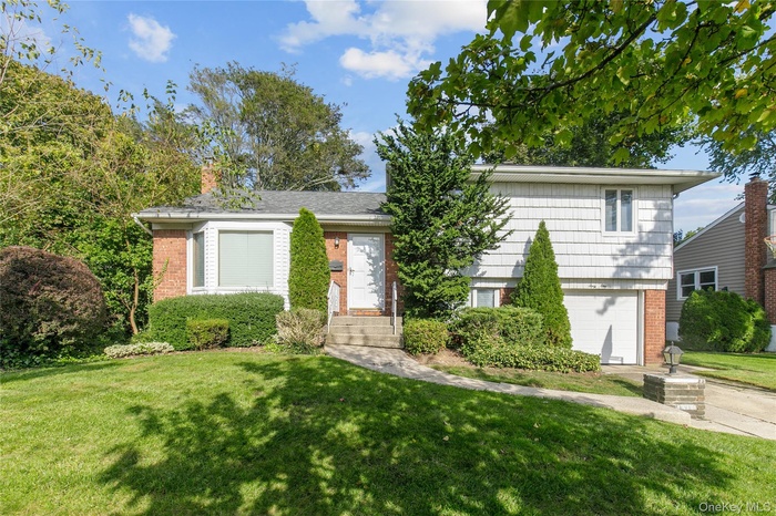Split level home with brick siding, an attached garage, a front yard, and a chimney