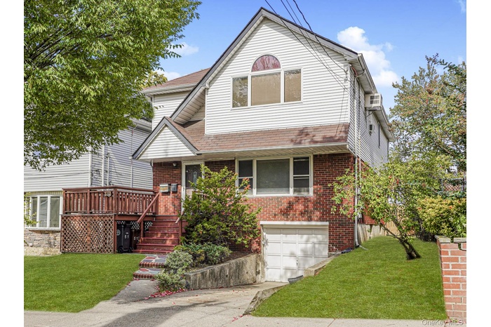View of front of house with a front yard, a wooden deck, driveway, and brick siding