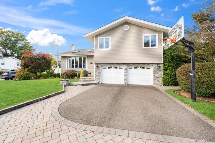 Tri-level home with stone siding, asphalt driveway, a front yard, a chimney, and an attached garage