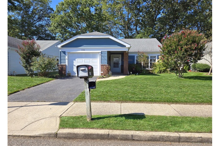 View of front facade with asphalt driveway, a front lawn, brick siding, roof with shingles, and an attached garage