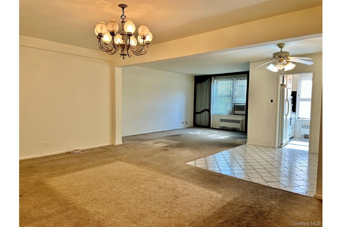 Carpeted spare room featuring tile patterned flooring, radiator heating unit, a chandelier, and a ceiling fan