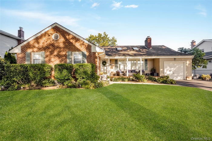 View of front of home with a front yard, an attached garage, brick siding, a chimney, and driveway