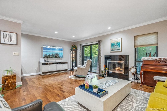 Living area featuring ornamental molding, wood finished floors, a glass covered fireplace, and recessed lighting
